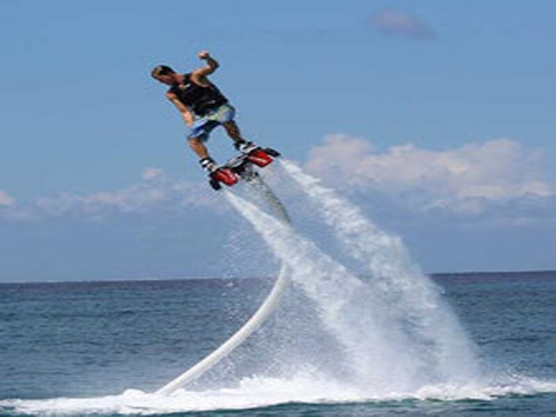 Homme en flyboard s'élève au-dessus de la mer, propulsé par de puissants jets d'eau sous ses pieds.