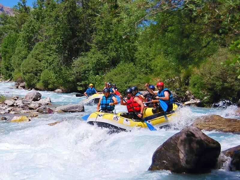 Groupe de six personnes en raft jaune pagayant dans une rivière avec des rapides et des rochers.