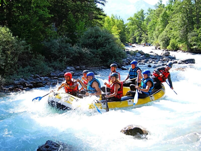 Six personnes en raft jaune pagayant dans une rivière de montagne avec des arbres et rochers autour.