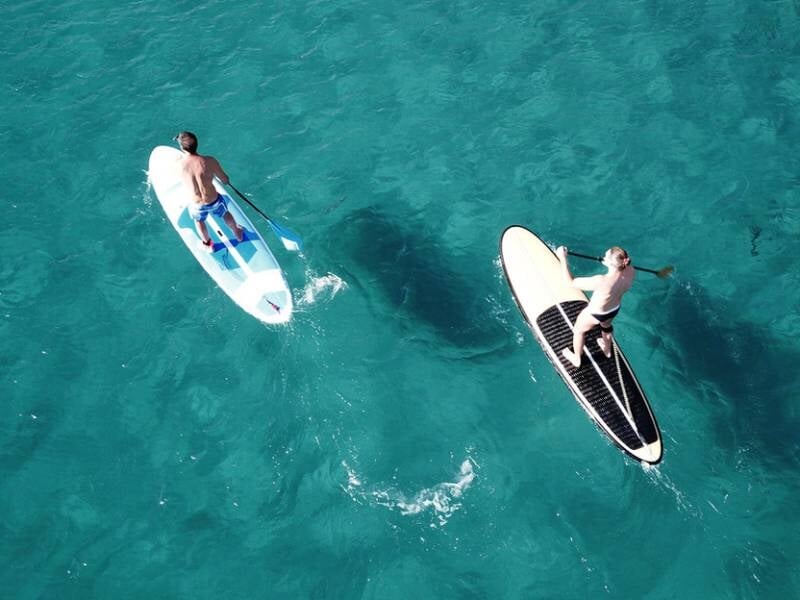 Vue aérienne de deux personnes sur des planches de stand-up paddle sur une eau turquoise claire.