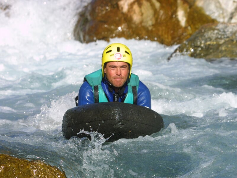 Homme en casque jaune pratiquant l'hydrospeed dans une rivière à eau vive entre des rochers.