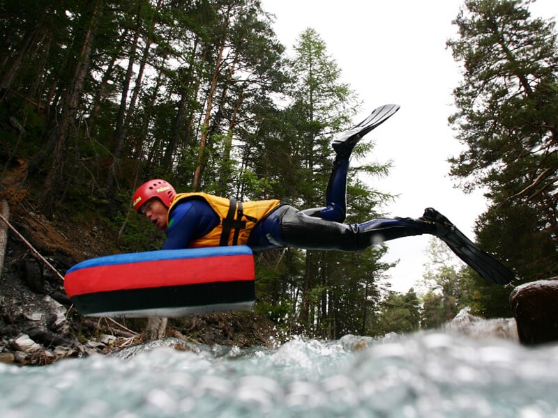 Personne en combinaison et casque rouge sautant dans une rivière avec un flotteur d'hydrospeed.