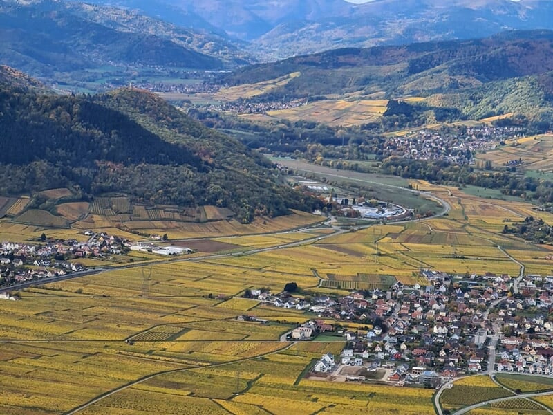 Vue aérienne d'un paysage vallonné avec des champs et un village sous un ciel clair en automne.