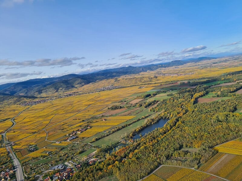 Paysage vu du ciel avec des champs jaunes, des collines et un lac entouré de végétation verte.