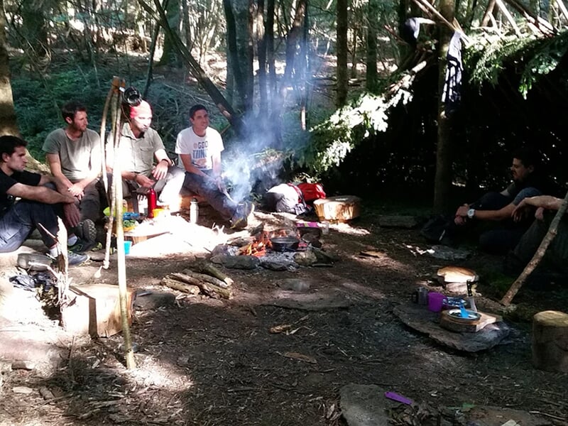 Groupe de personnes assises autour d'un feu de camp dans une clairière forestière, partageant un moment.