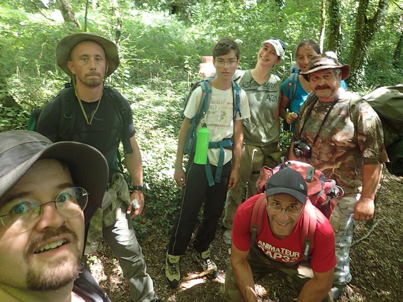 Groupe de randonneurs posant pour une photo dans une forêt, souriants et équipés de sacs à dos.