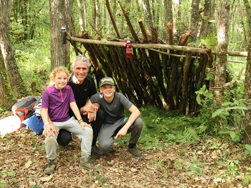 Groupe de personnes posant joyeusement dans une forêt, certains tenant des bâtons, ambiance conviviale.