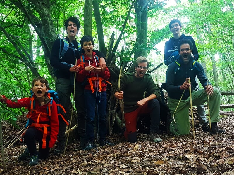 Groupe de personnes assises dans une cabane en bois faite de branches, souriantes et détendues.