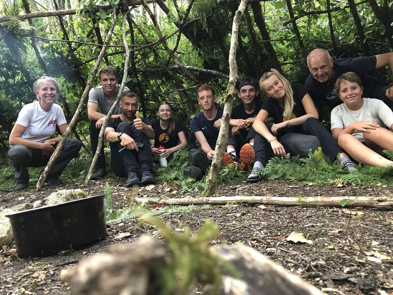 Groupe de personnes assises en cercle dans une forêt, partageant un moment autour d'un feu de camp.