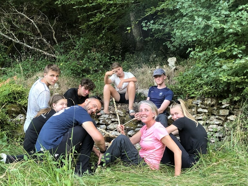 Groupe de personnes posant joyeusement dans une forêt, certains tenant des bâtons, ambiance conviviale.