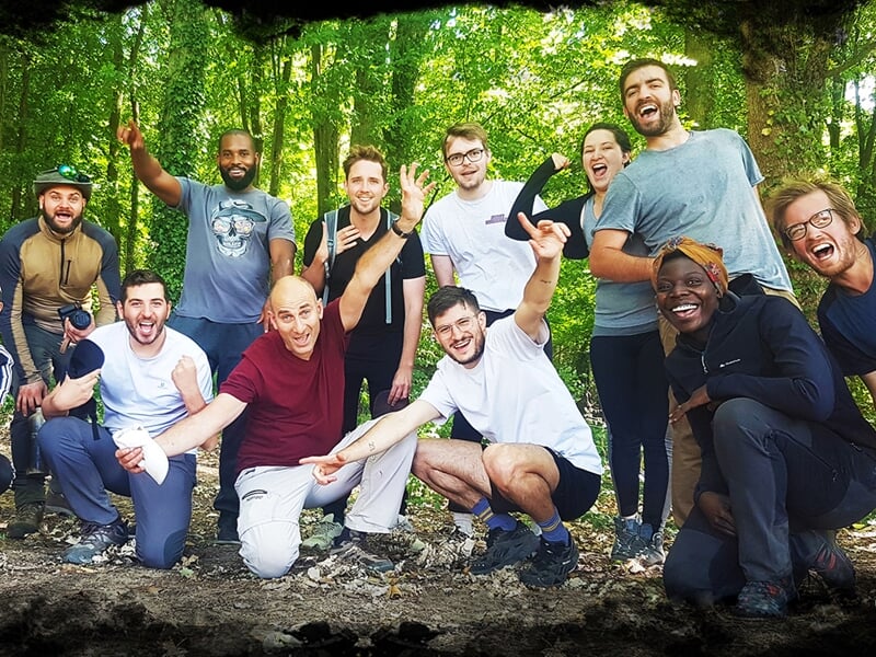 Groupe de personnes assises dans une cabane en bois faite de branches, souriantes et détendues.