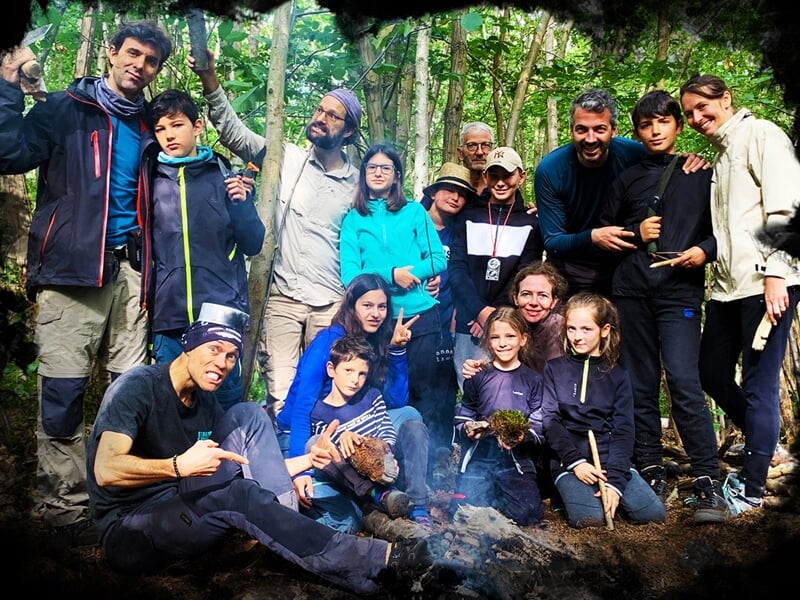 Groupe de personnes posant joyeusement dans une forêt, certains tenant des bâtons, ambiance conviviale.