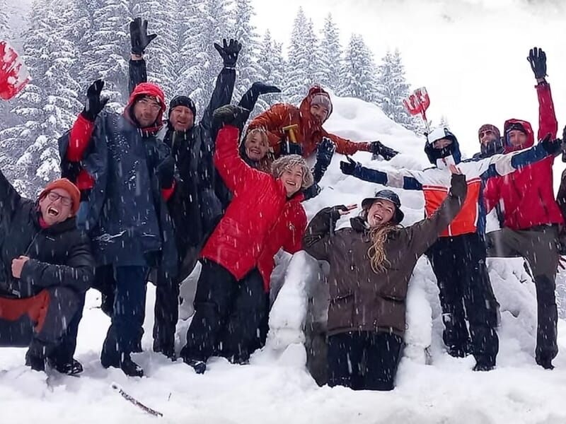 Groupe de personnes en tenue d'hiver posant joyeusement dans la neige lors d'un stage de survie en hiver dans le Haut-Jura.