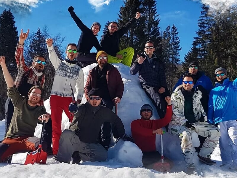 Dix personnes souriantes en vêtements d'hiver posent devant un igloo lors d'un stage de survie en hiver dans le Haut-Jura.