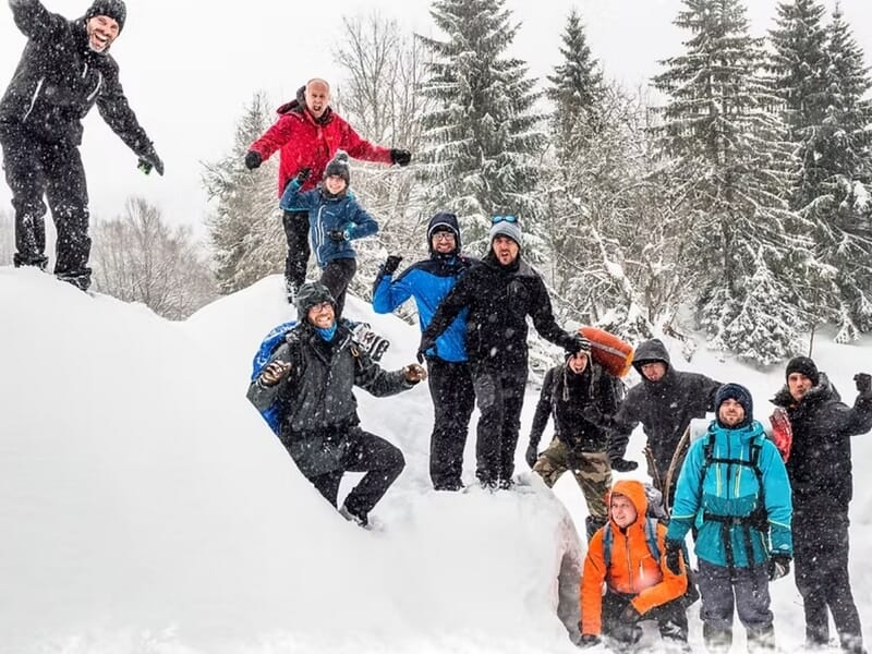 Groupe de treize personnes en tenue de neige posant sur un monticule enneigé lors d'un stage de survie en hiver dans le Haut-Jura.