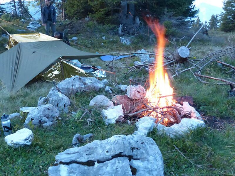 Feu de camp allumé au milieu de pierres dans un environnement montagneux avec une tente verte à proximité.