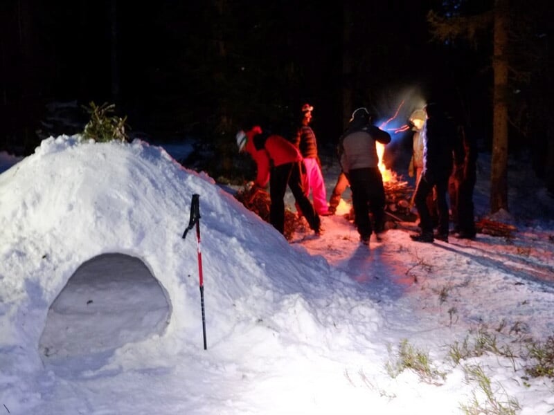 Un igloo en neige est construit près d'un groupe de personnes autour d'un feu de camp dans la nuit.