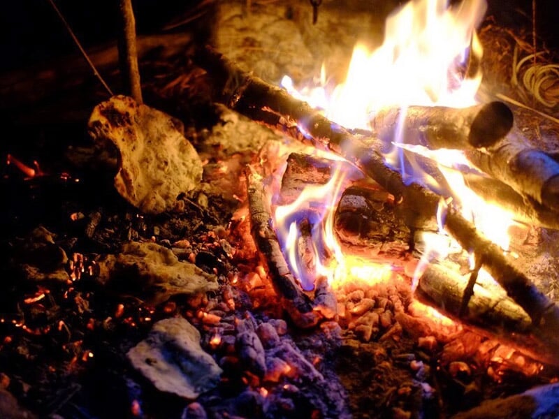 Feu de camp avec des braises rouges et des morceaux de bois brûlant dans un environnement naturel.