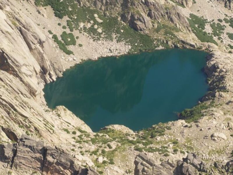 Lac de montagne aux eaux turquoise, entouré de roches escarpées et de végétation clairsemée. Paysage sauvage et isolé en altitude.