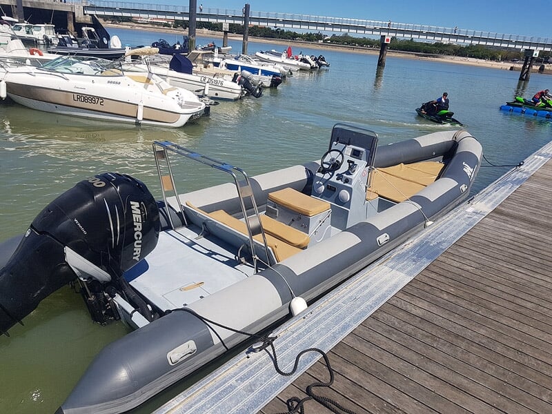 Un bateau pneumatique gris avec moteur Mercury est amarré à un ponton en bois dans un port.