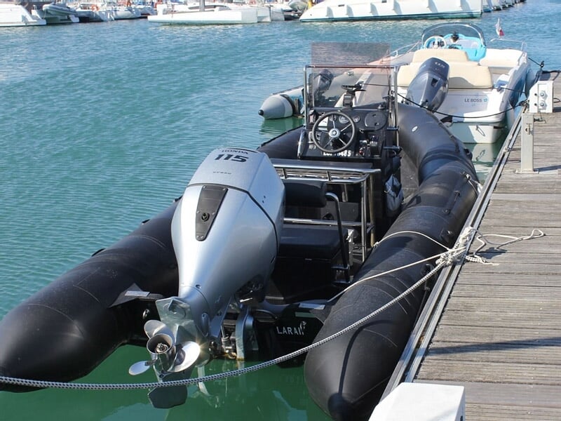 Un bateau pneumatique noir avec moteur Mercury est amarré dans un port, vu de l'arrière.