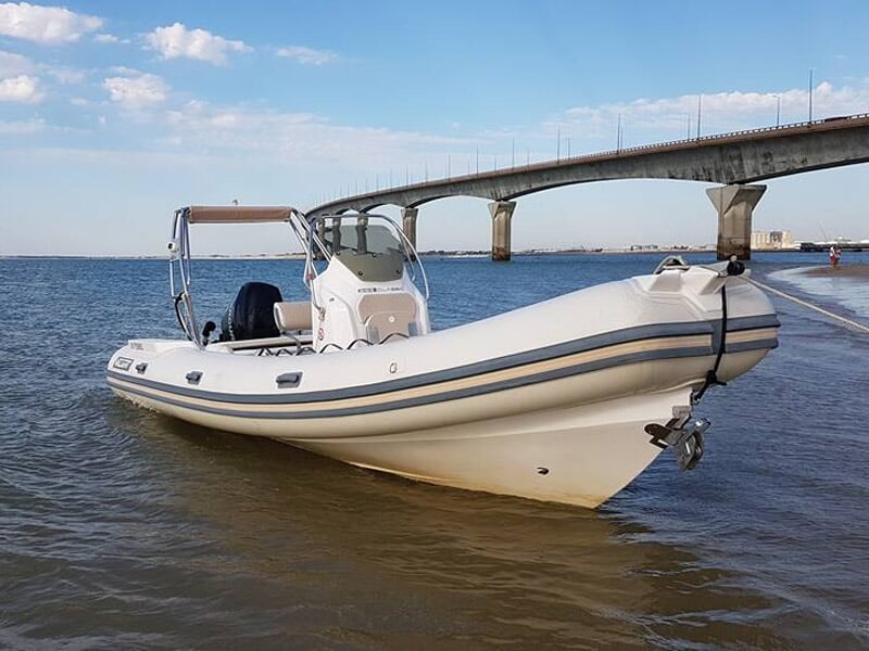 Un bateau pneumatique blanc est amarré près d'un ponton avec un pont et un ciel bleu en arrière-plan.