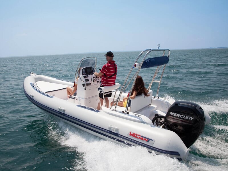 Deux personnes naviguent sur un bateau pneumatique blanc avec moteur Mercury sur une mer calme.