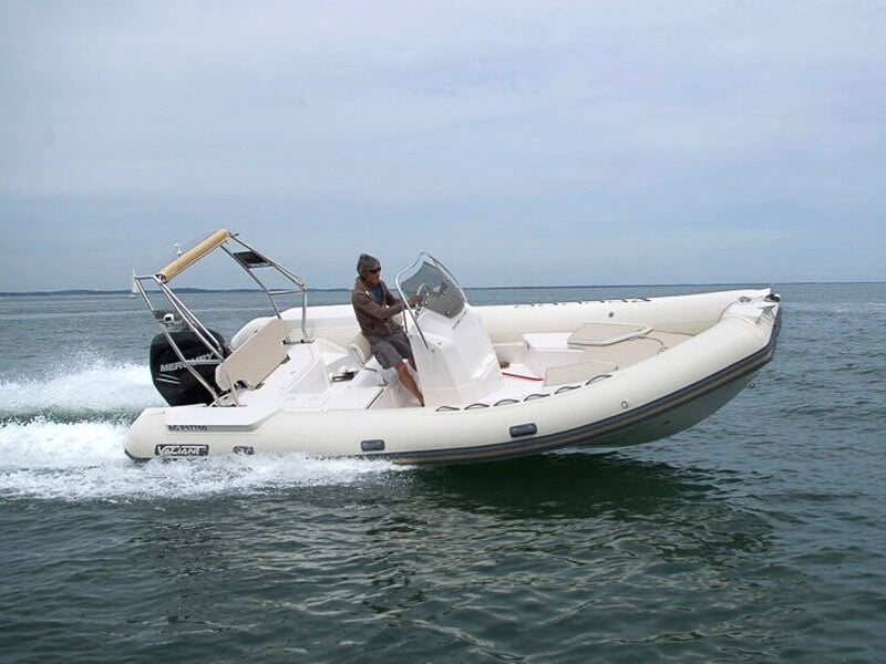 Un homme conduit un bateau pneumatique blanc sur une mer calme sous un ciel bleu clair.