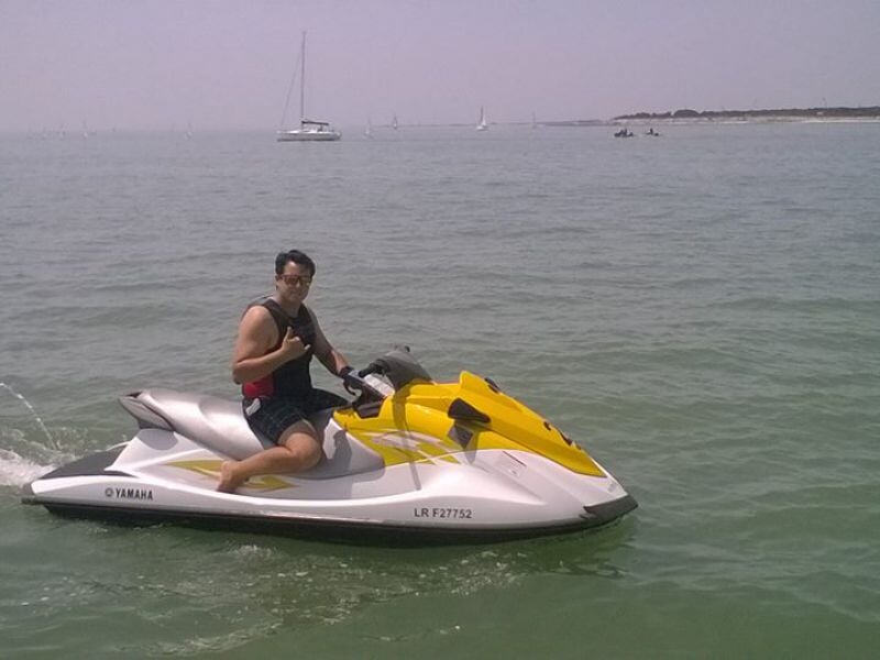 Un homme en gilet de sauvetage rouge sur un jetski blanc et jaune navigue sur une mer calme.