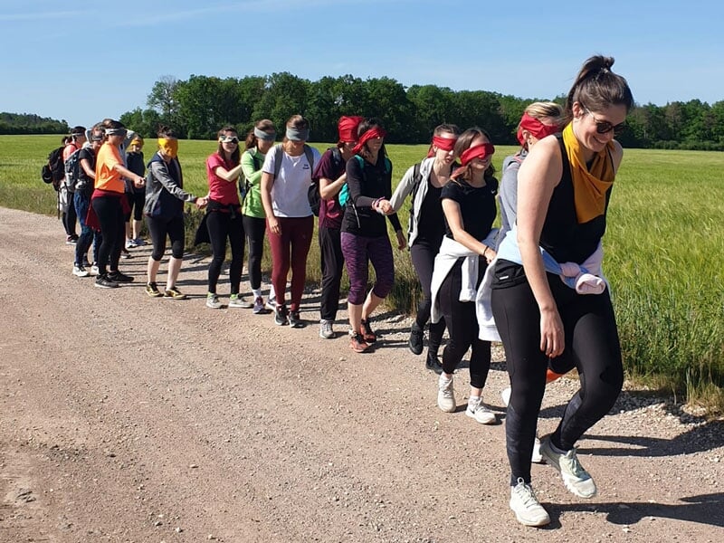 un groupe de personnes font une épreuve les yeux bandés sur une route de campagne