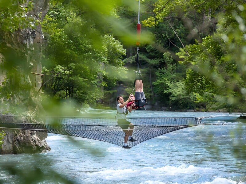 Atterrissage sécurisé d'une participante sur un filet tendu au-dessus d'une rivière, encadrée par un membre de l'équipe. L'environnement naturel ajoute une touche apaisante à l'expérience