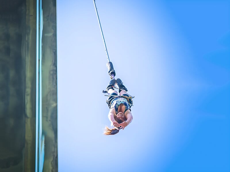 Femme en position inversée durant un saut à l'élastique, câble tendu, ciel parfaitement dégagé. Illustration dynamique d'une aventure sportive