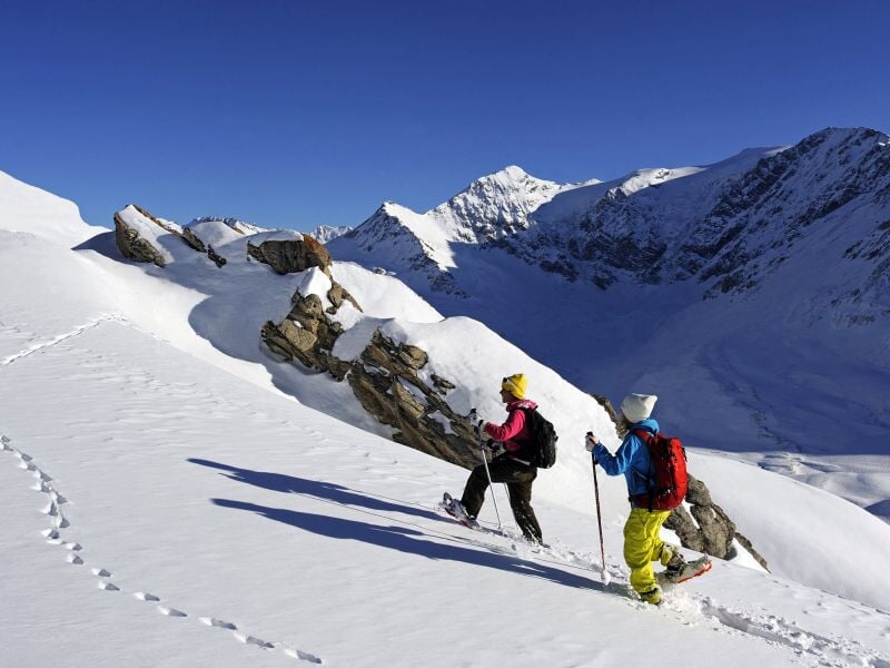 Deux randonneurs en raquettes progressant sur un sentier enneigé en montagne avec un ciel clair et ensoleillé.