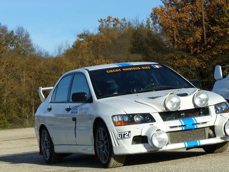 Voiture de rallye blanche avec des phares supplémentaires garée sur une route goudronnée en forêt