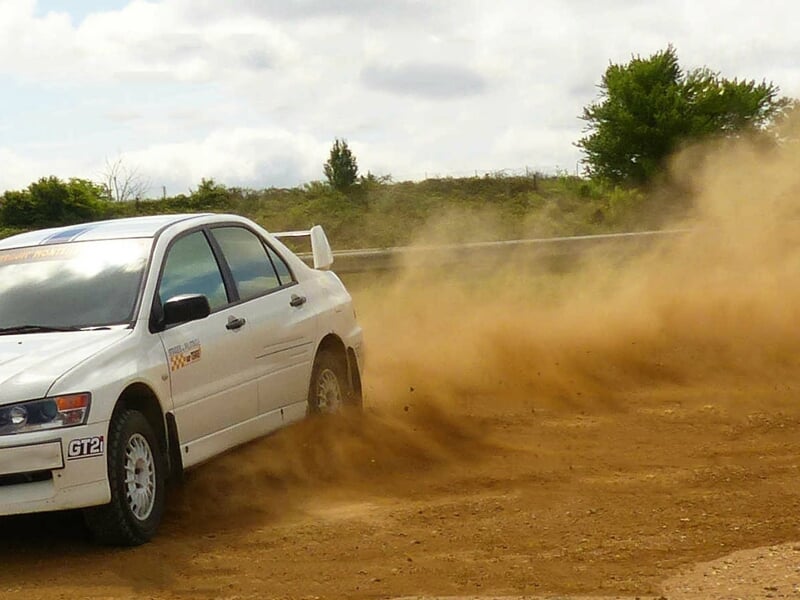 Voiture de rallye blanche dérapant sur une piste de terre, soulevant un nuage de poussière