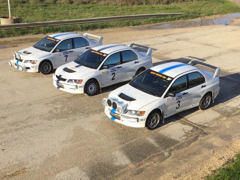Trois voitures de rallye blanches alignées sur une surface goudronnée avec des numéros sur les portières