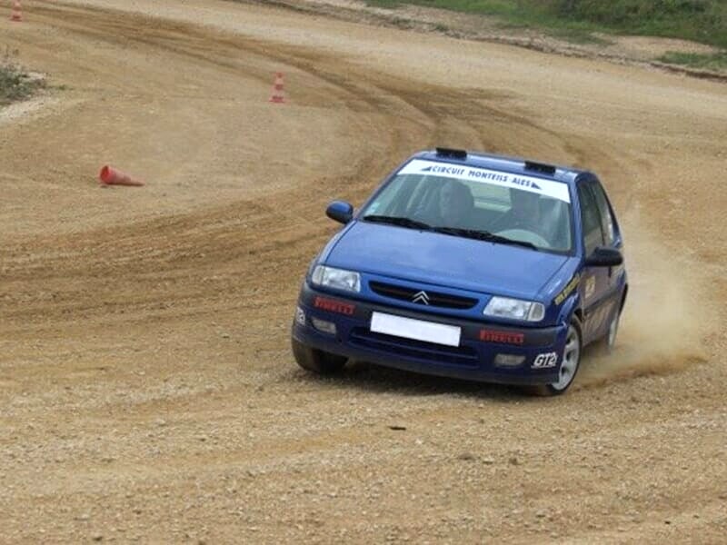 Voiture de rallye bleue sur une piste de terre, en train de tourner avec de la poussière soulevée