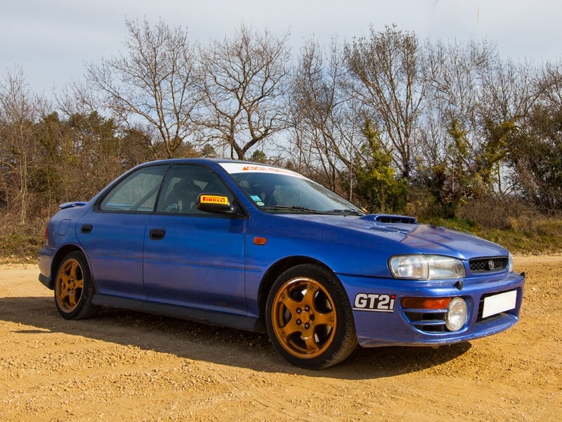 Voiture de rallye bleue avec jantes dorées stationnée sur une piste de terre