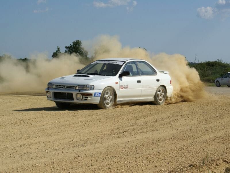 Voiture de rallye blanche dérapant sur une piste de terre, soulevant un nuage de poussière