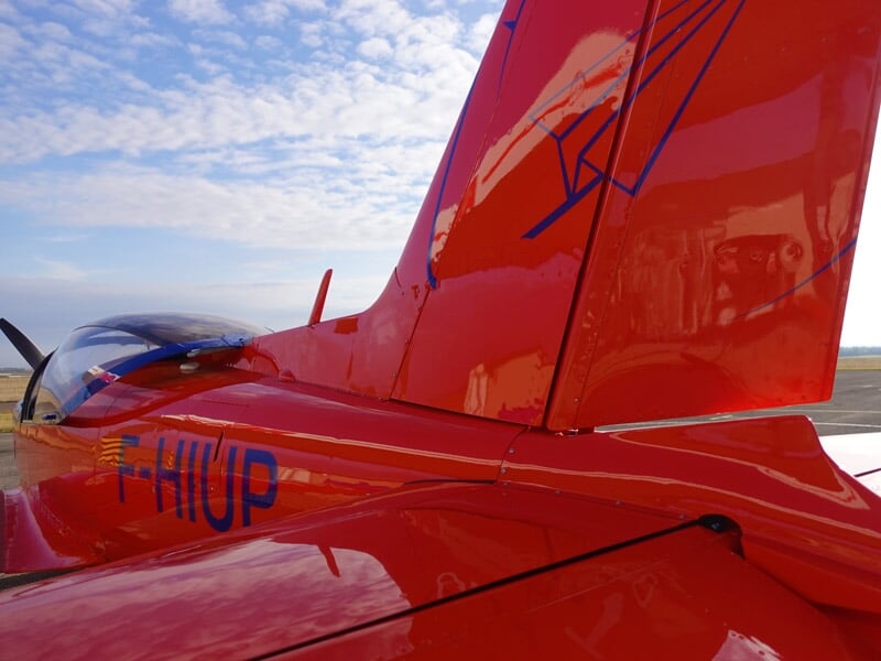 Gros plan sur la queue rouge vif d'un avion avec l'immatriculation F-HIUP visible au soleil.