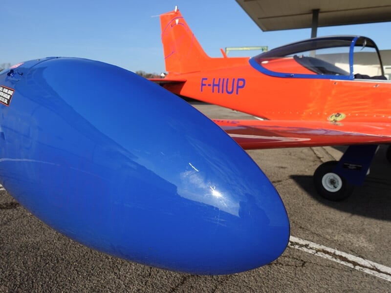 Détail de l'aile bleue et du train d'atterrissage d'un avion rouge stationné sur l'asphalte.