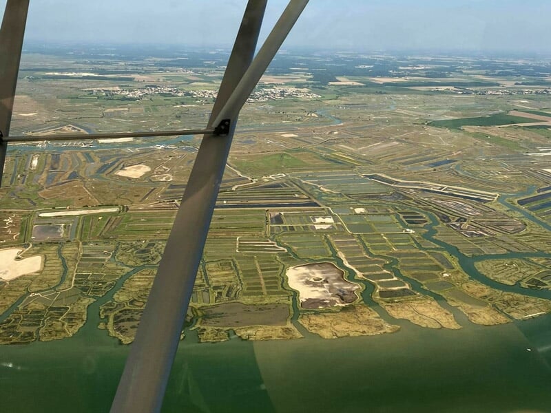 Paysage vu depuis un avion ULM montrant des terres agricoles et des marais avec un ciel bleu clair.
