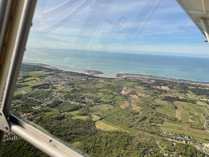 Vue depuis un avion ULM montrant une ville côtière avec plages et forêt en arrière-plan.