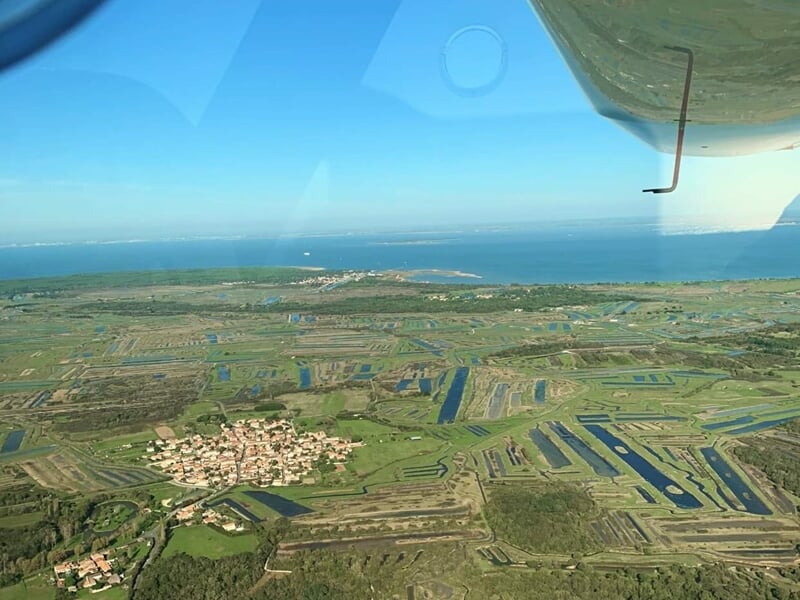 Paysage vu d'un avion ULM avec terres agricoles, marais et océan à l'horizon.
