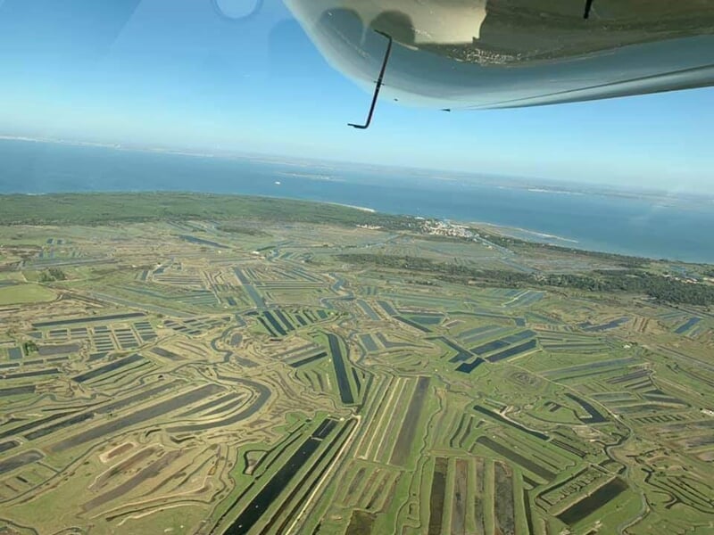 Vue aérienne d'un paysage de marais et terres cultivées avec un ciel bleu clair.