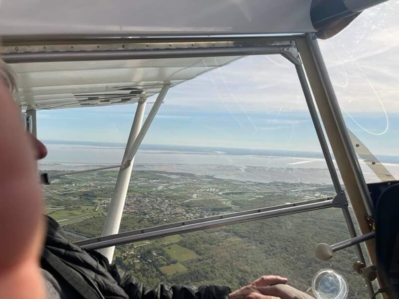 Personne à bord d'un avion ULM regardant à travers la fenêtre avec paysage rural en vue.