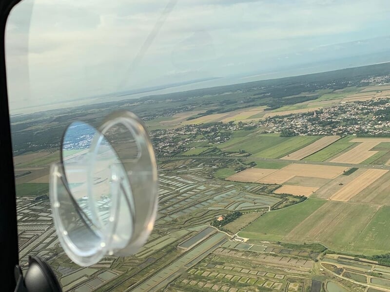 Vue aérienne prise depuis un avion montrant des champs cultivés et des villages sous un ciel clair.