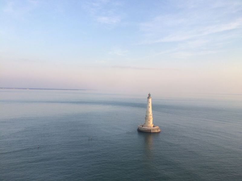Vue aérienne d'un phare isolé au milieu de la mer sous un ciel clair au coucher du soleil.