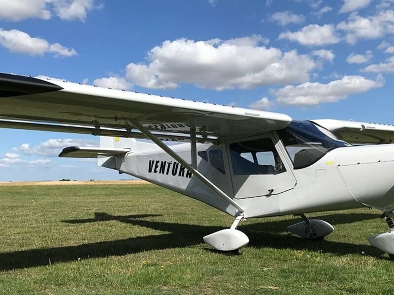 Petit avion blanc stationné sur un terrain d'herbe verte sous un ciel bleu initiation ULM près de Fontainebleau.