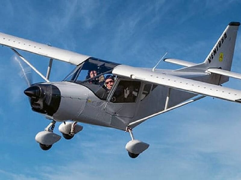 Avion léger blanc en vol avec un pilote visible initiation ULM près de Fontainebleau.